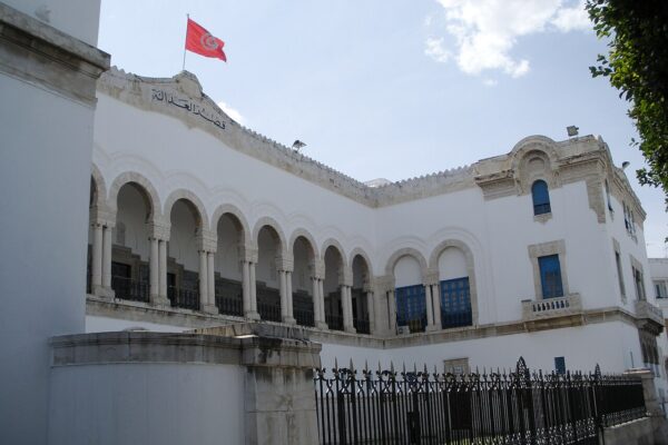 White courthouse in Tunis with arched gallery, blue shutters and a Tunisian flag, Arabic lettering reading Palace of Justice