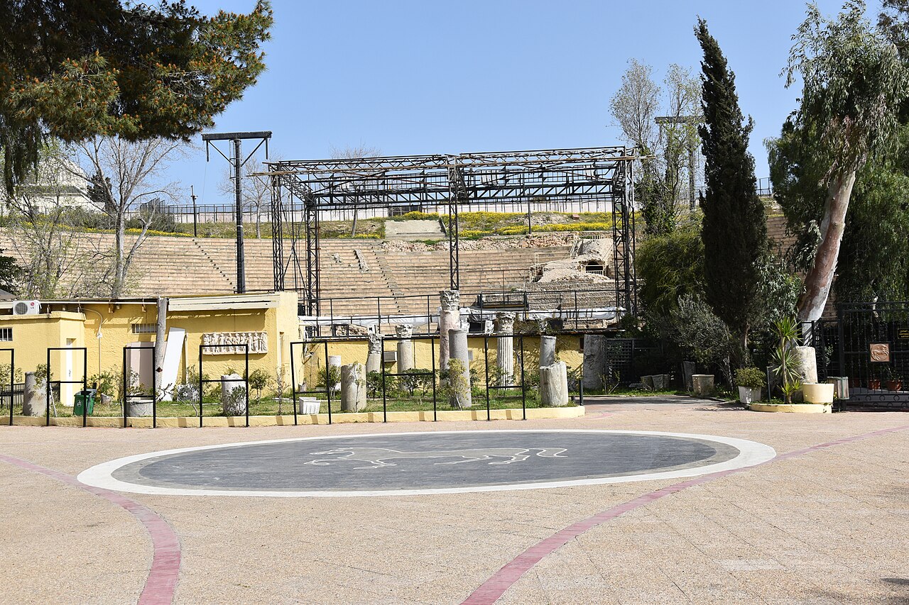 Stone seating of the Roman theatre of Carthage rising behind a paved plaza with ancient columns and a metal stage frame, where the Carthage International Festival is held