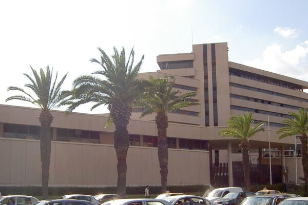Beige multi-storey headquarters of the Central Bank of Tunisia in Tunis behind a row of palm trees and parked cars