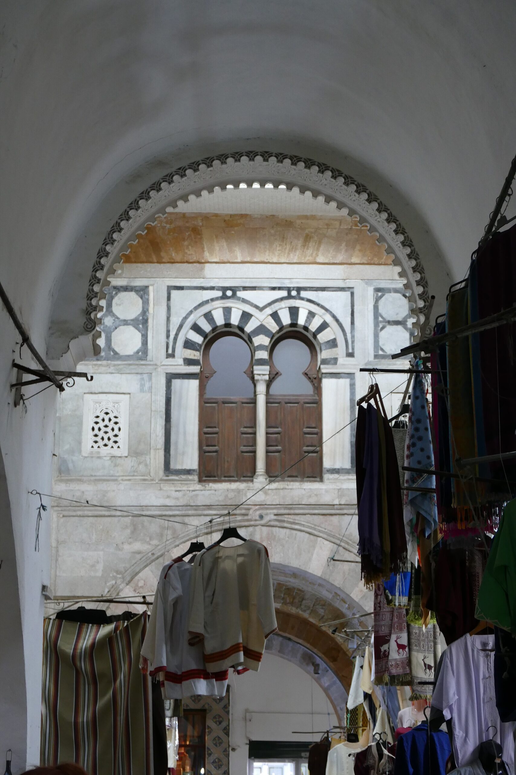 A vaulted covered souq passage in the Tunis medina with hanging clothes and an arched marble window