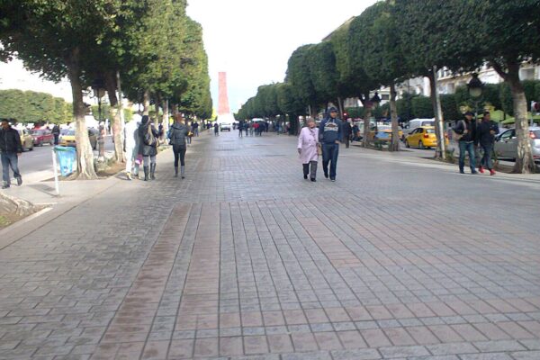 Pedestrians and taxis on the tree-lined Avenue Habib Bourguiba in central Tunis, with a tower in the distance
