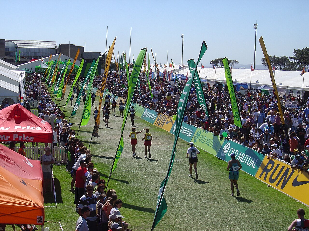 Runners and a large crowd at the finish area of the Two Oceans Marathon on the University of Cape Town campus, with sponsor banners and tents.