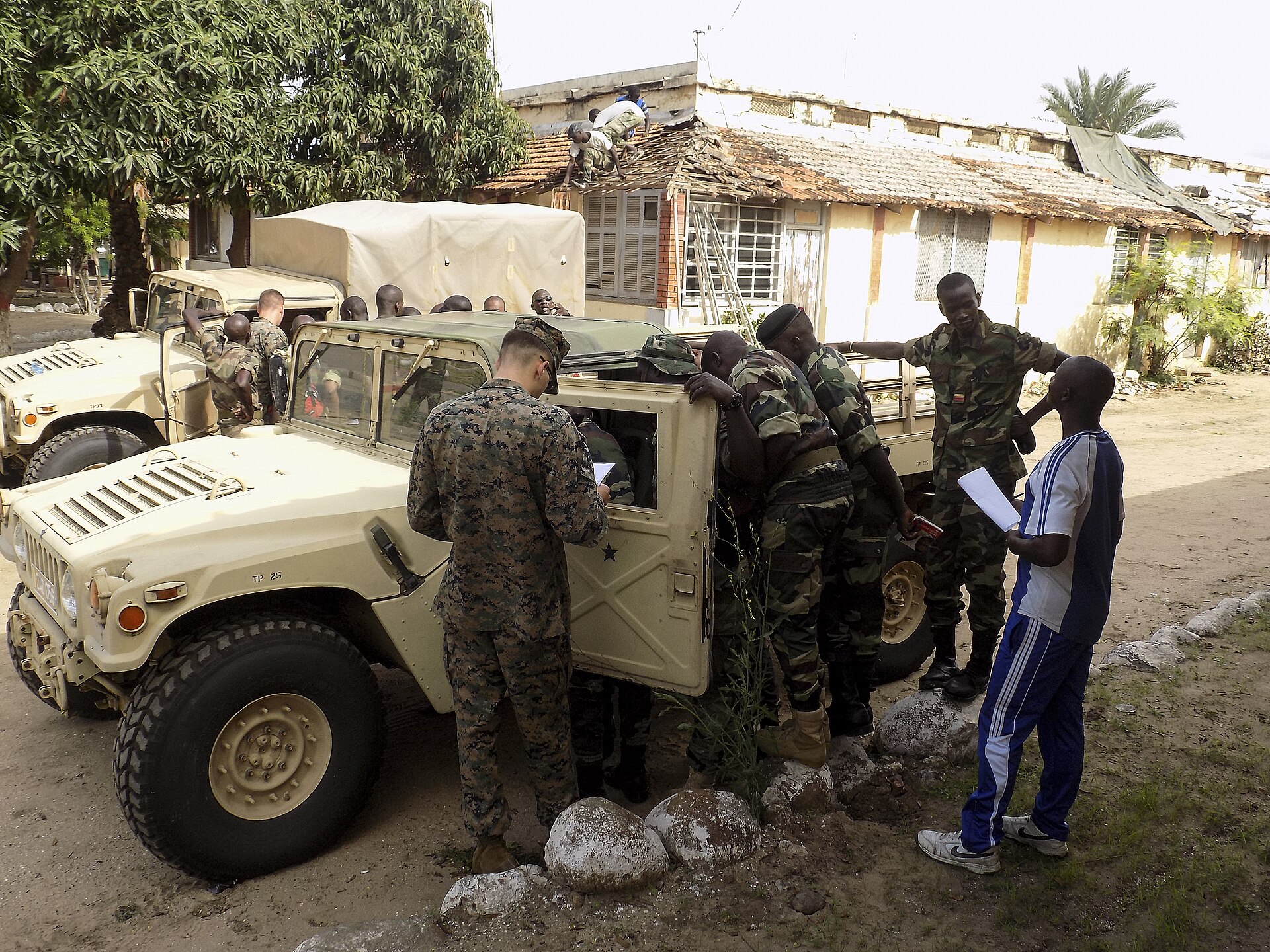 A US Marine and Senegalese gendarmes in camouflage uniforms gather around an open Humvee door in a yard