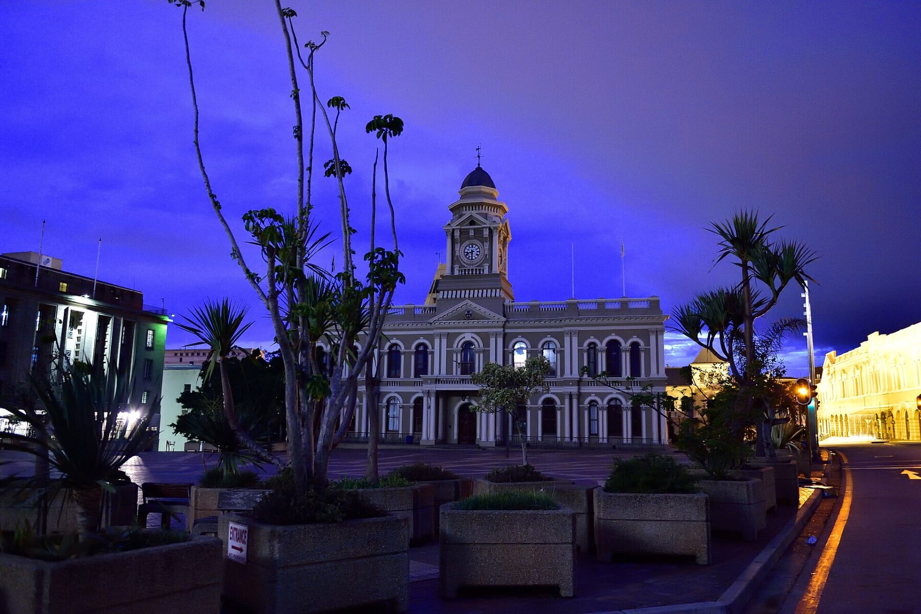 Port Elizabeth City Hall, a white colonial-era building with a clock tower, lit at dusk behind a square with planters and palm trees