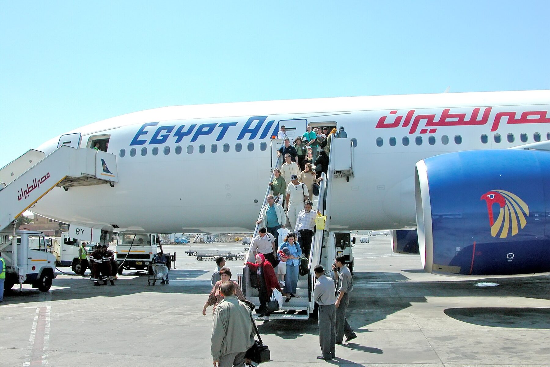 Passengers walk down the stairs of a white EgyptAir aircraft with the airline's falcon logo, parked on the apron at Cairo International Airport