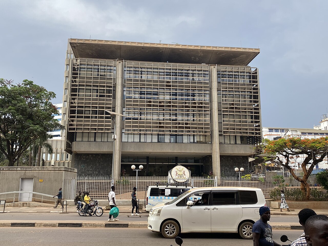 The Bank of Uganda building in Kampala, a concrete office block with the national coat of arms at its gate, with traffic and pedestrians in front