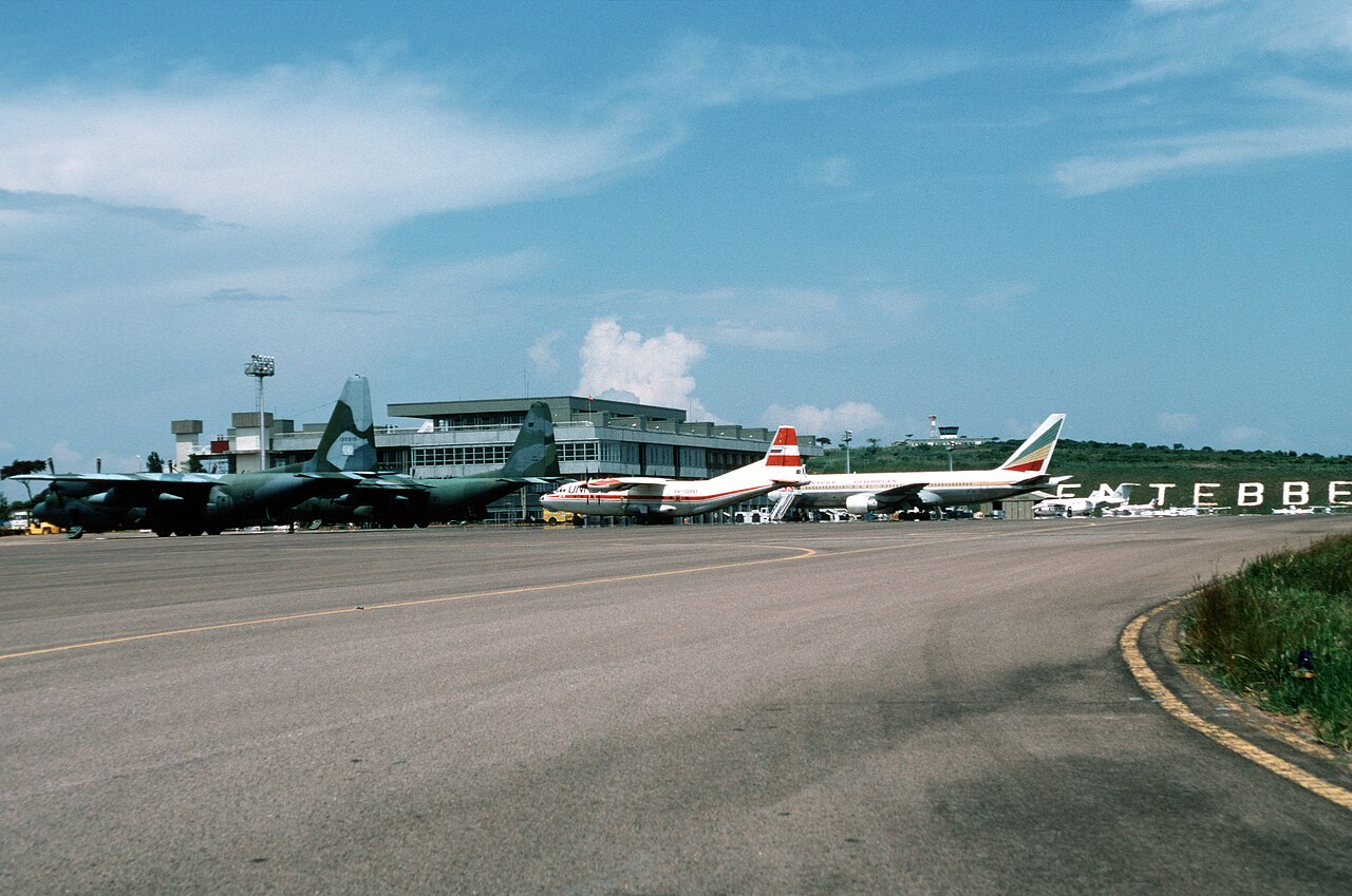 Two military transport aircraft and airliners parked in front of the terminal at Entebbe airport