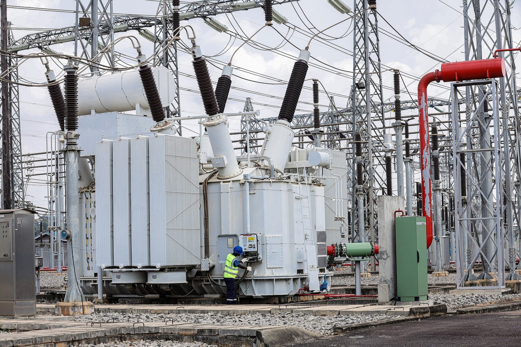 A technician in a hard hat and high-visibility vest checks a large transformer at the UETCL Lugogo substation in Kampala, Uganda