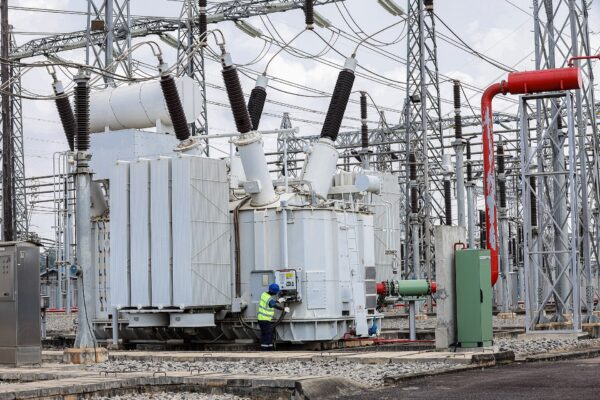 A technician in a hard hat and high-visibility vest checks a large transformer at the UETCL Lugogo substation in Kampala, Uganda