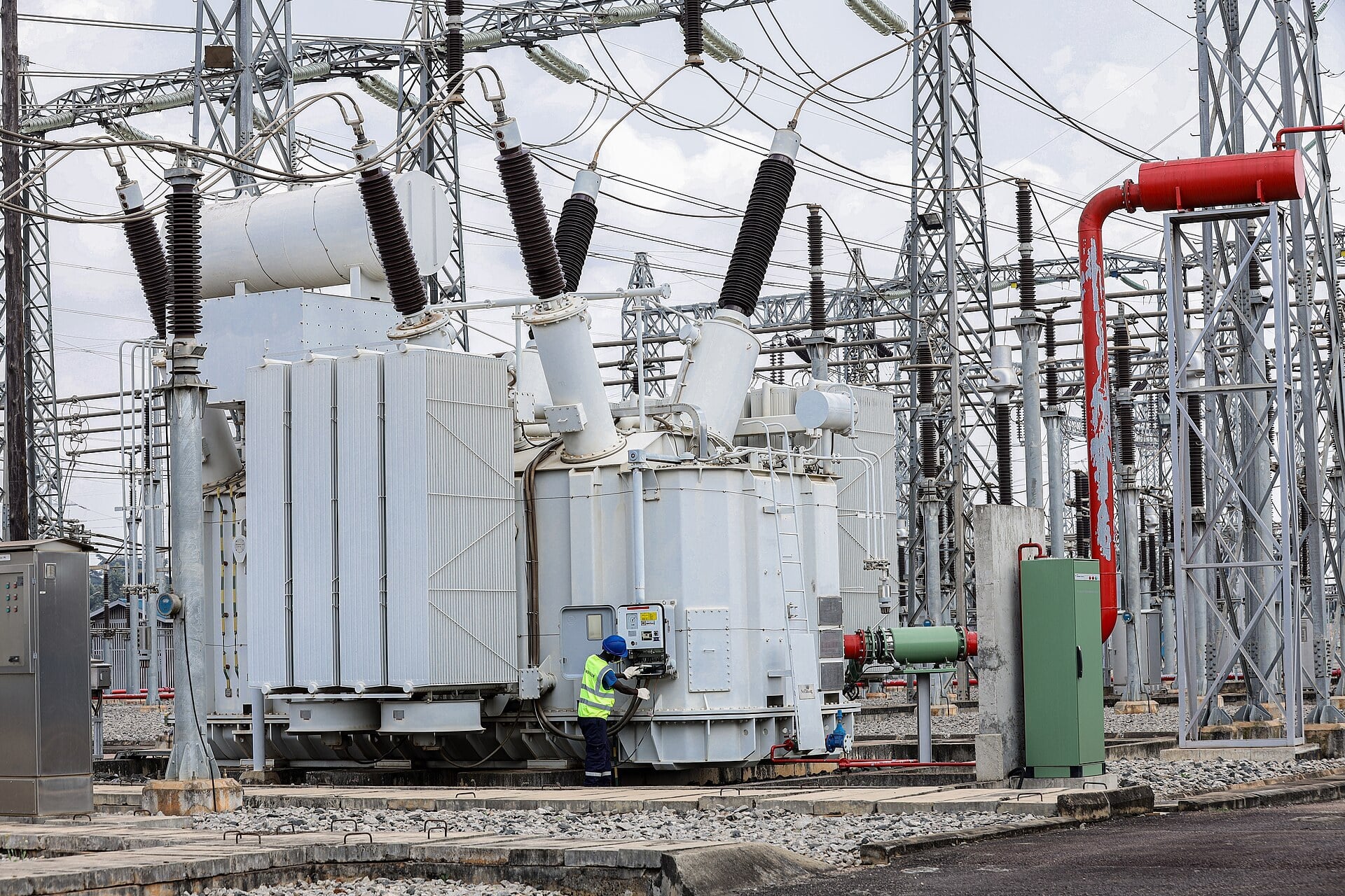 A technician in a hard hat and high-visibility vest checks a large transformer at the UETCL Lugogo substation in Kampala, Uganda