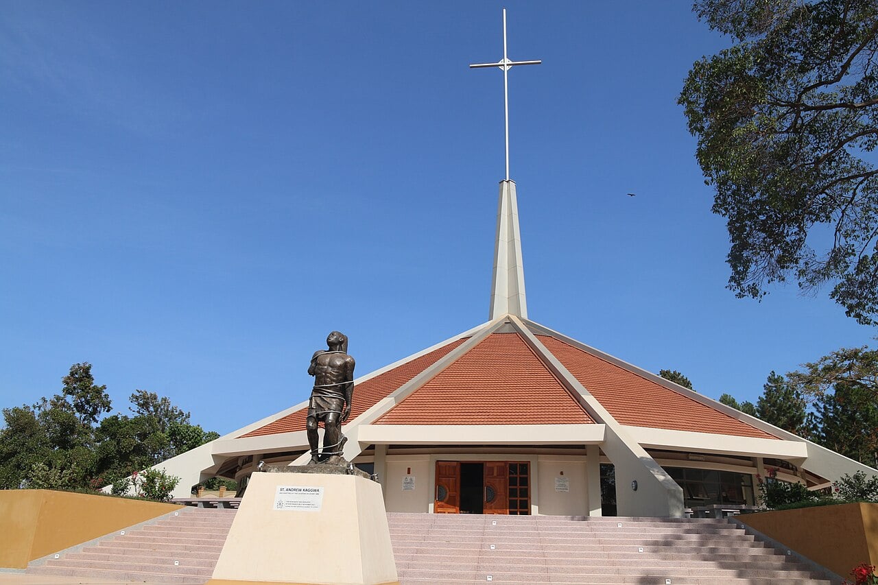 Munyonyo Martyrs Shrine church in Kampala with a tall white cross and a bronze statue in front