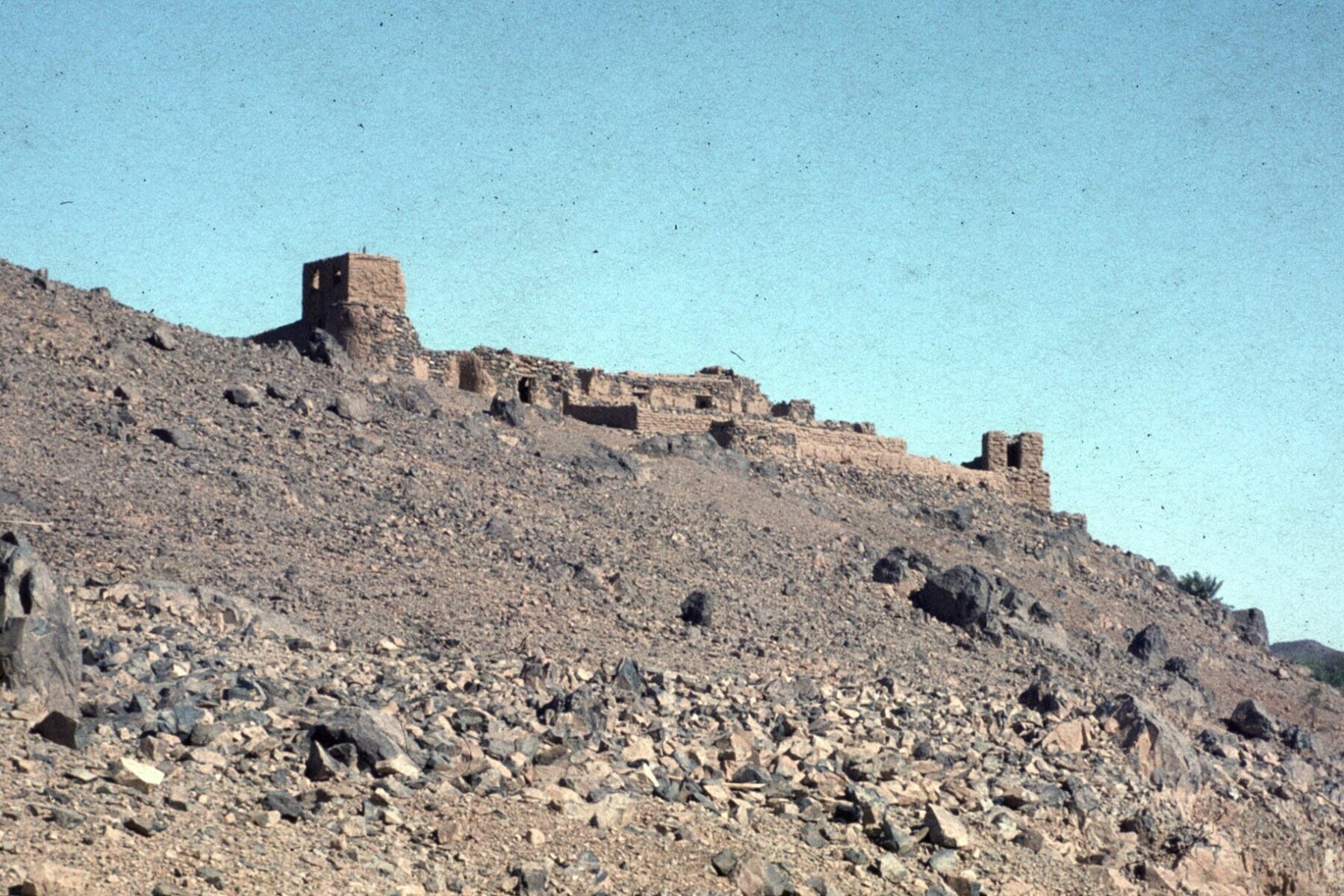 A ruined mud-brick fortress on a rocky hillside above the town of Tessalit in northern Mali under a clear sky