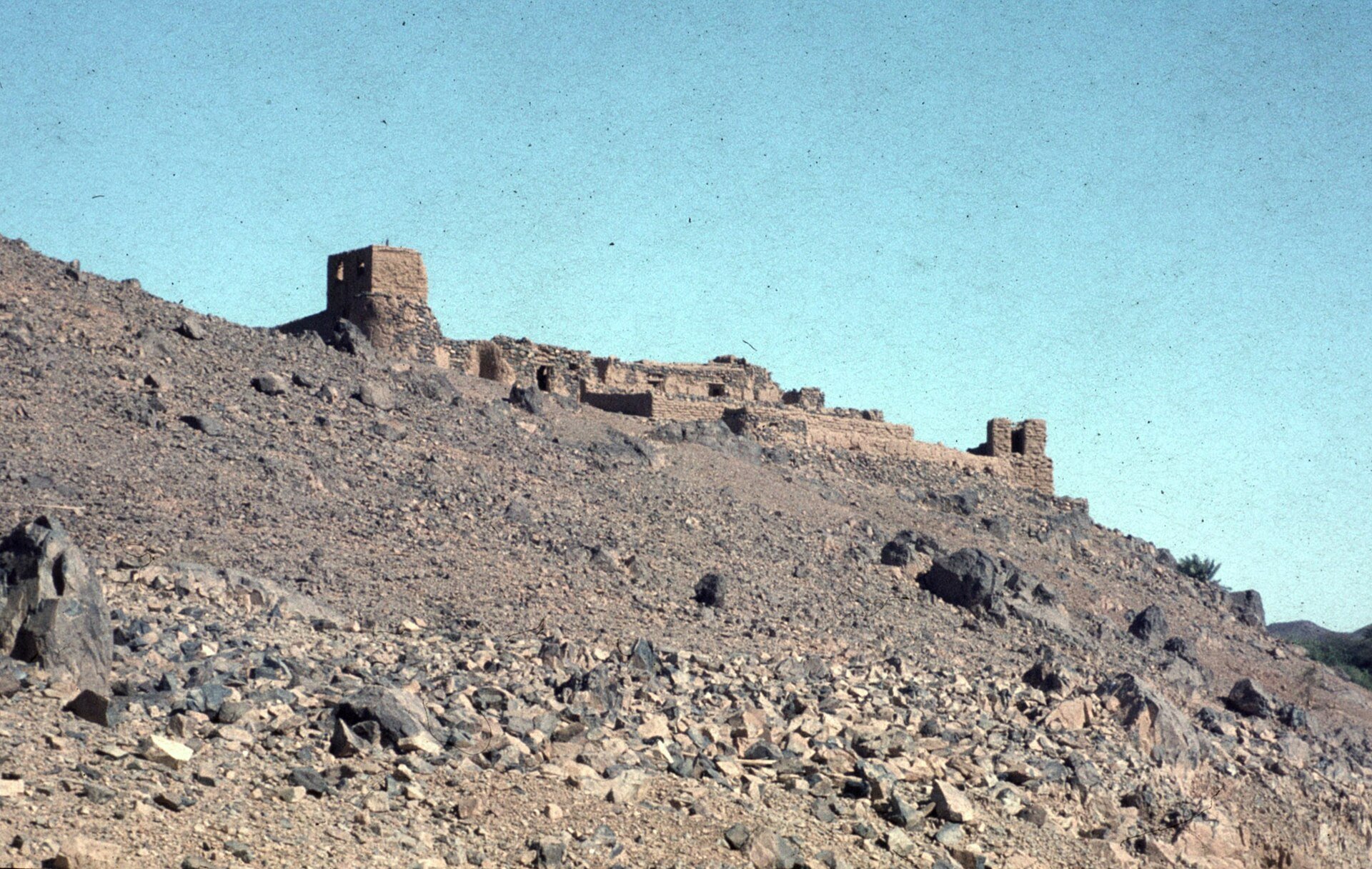A ruined mud-brick fortress on a rocky hillside above the town of Tessalit in northern Mali under a clear sky