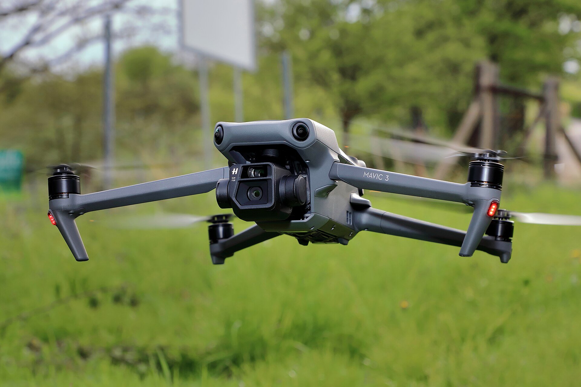 A grey DJI Mavic 3 commercial camera drone hovering in flight above a green meadow