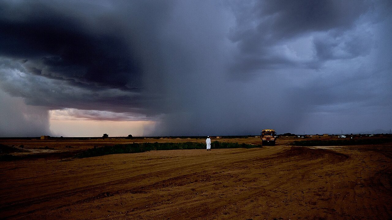 A rain storm over open ground near El Obeid in Kordofan, Sudan, with a lone man and a bus on the plain