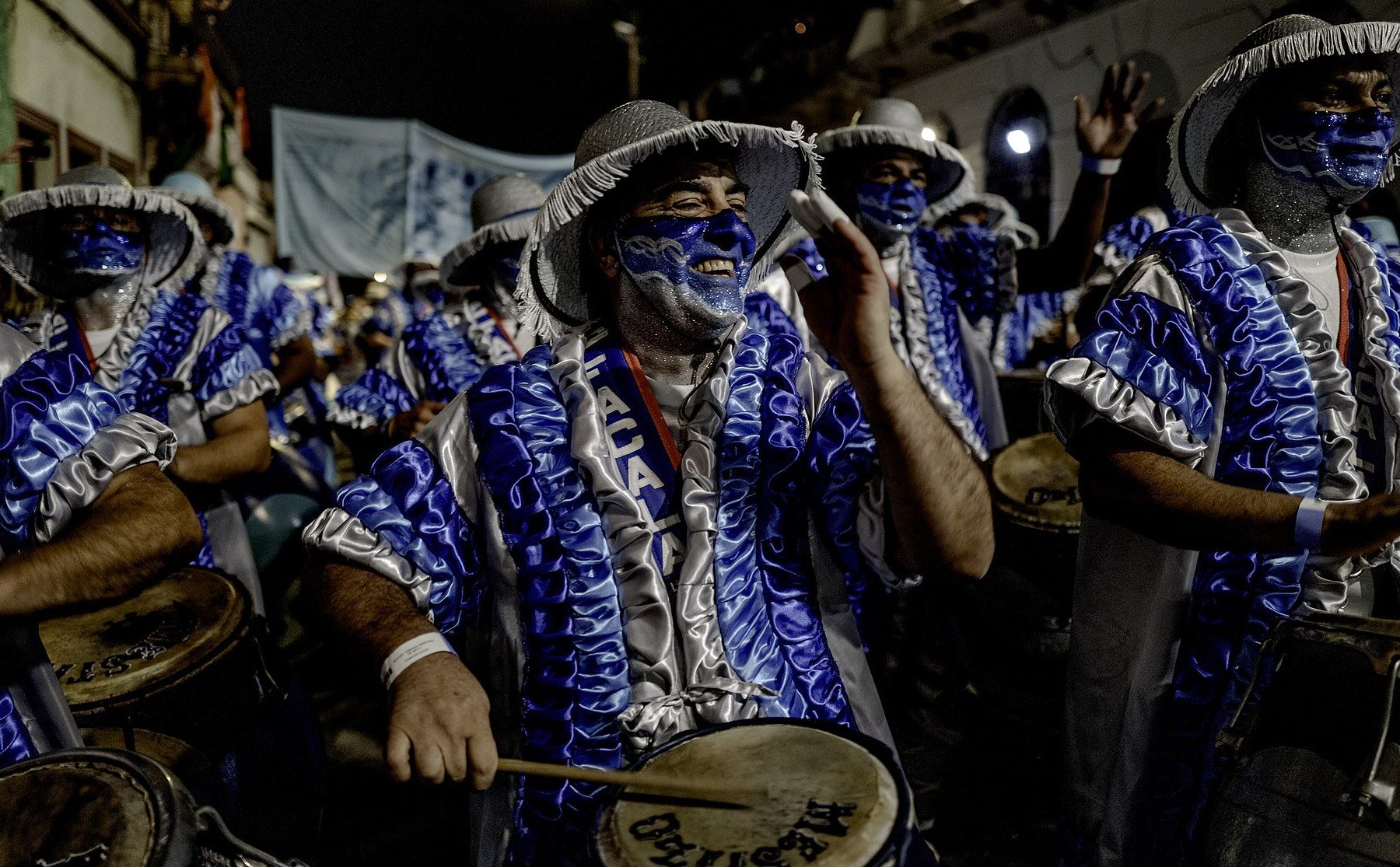 Candombe drummers in blue and silver costumes and face paint march at night in the Desfile de Llamadas in Barrio Sur, Montevideo