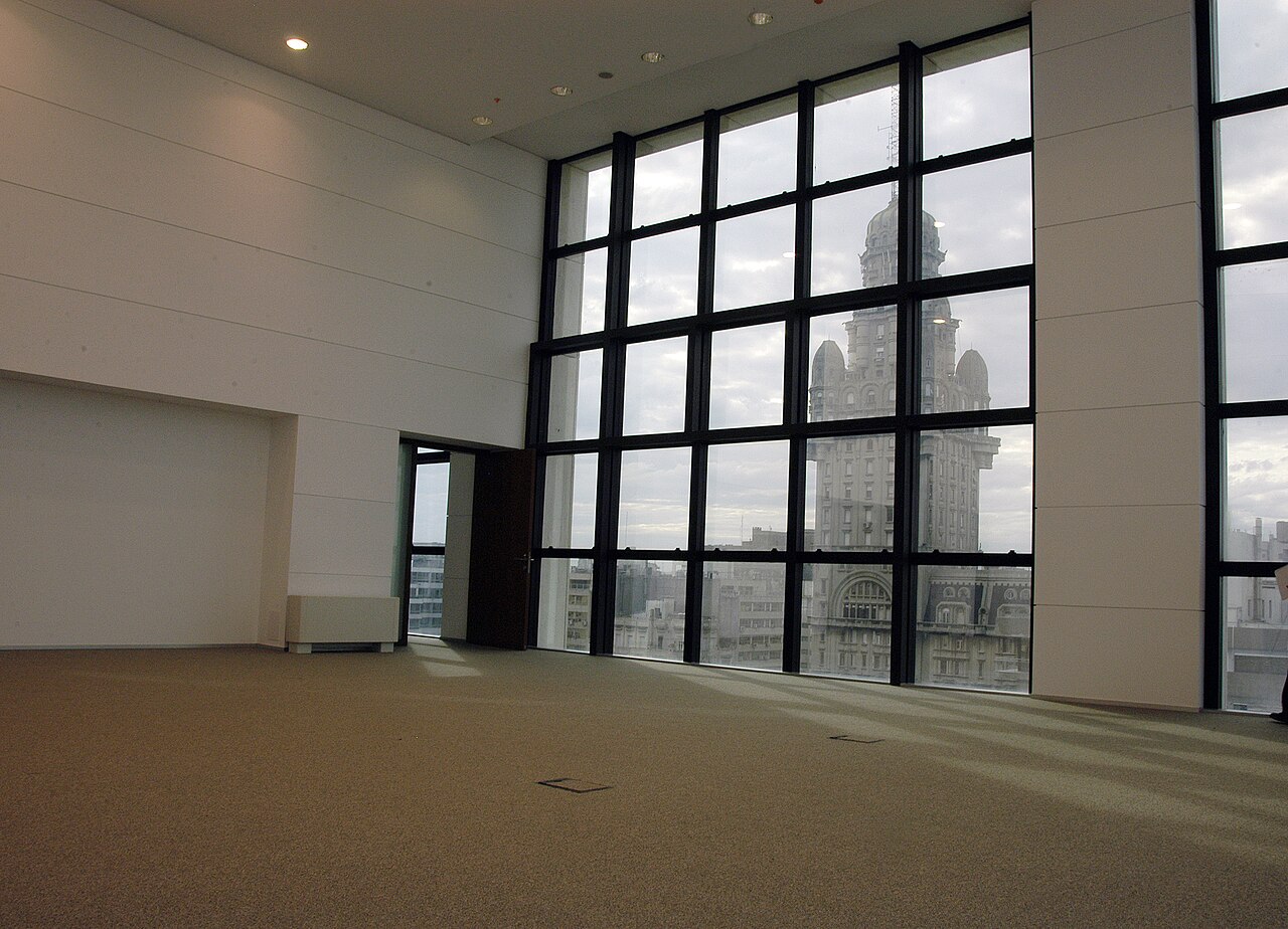 Empty high-ceilinged office floor with large windows looking out on the Palacio Salvo tower in Montevideo
