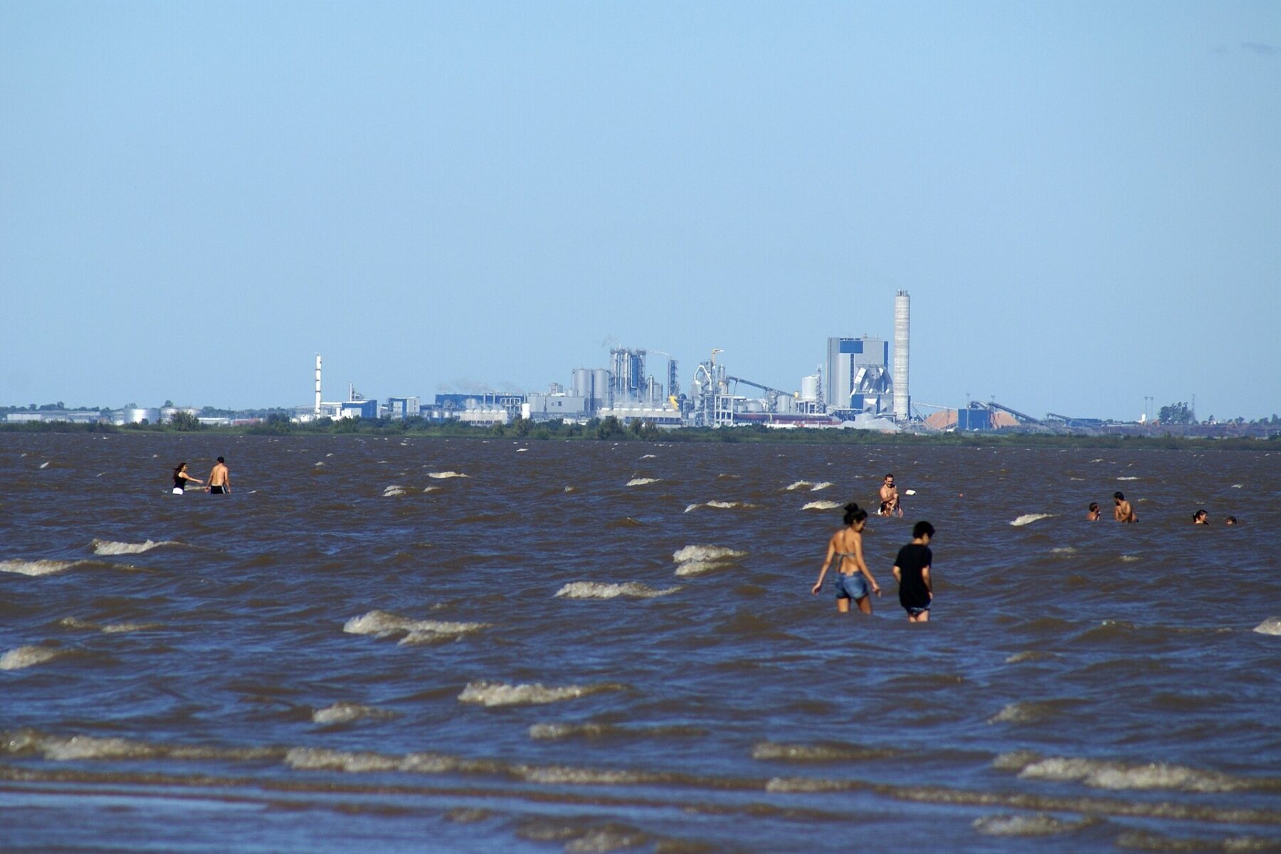 Pulp mill on the Uruguay River near Fray Bentos seen across the water with bathers in the foreground