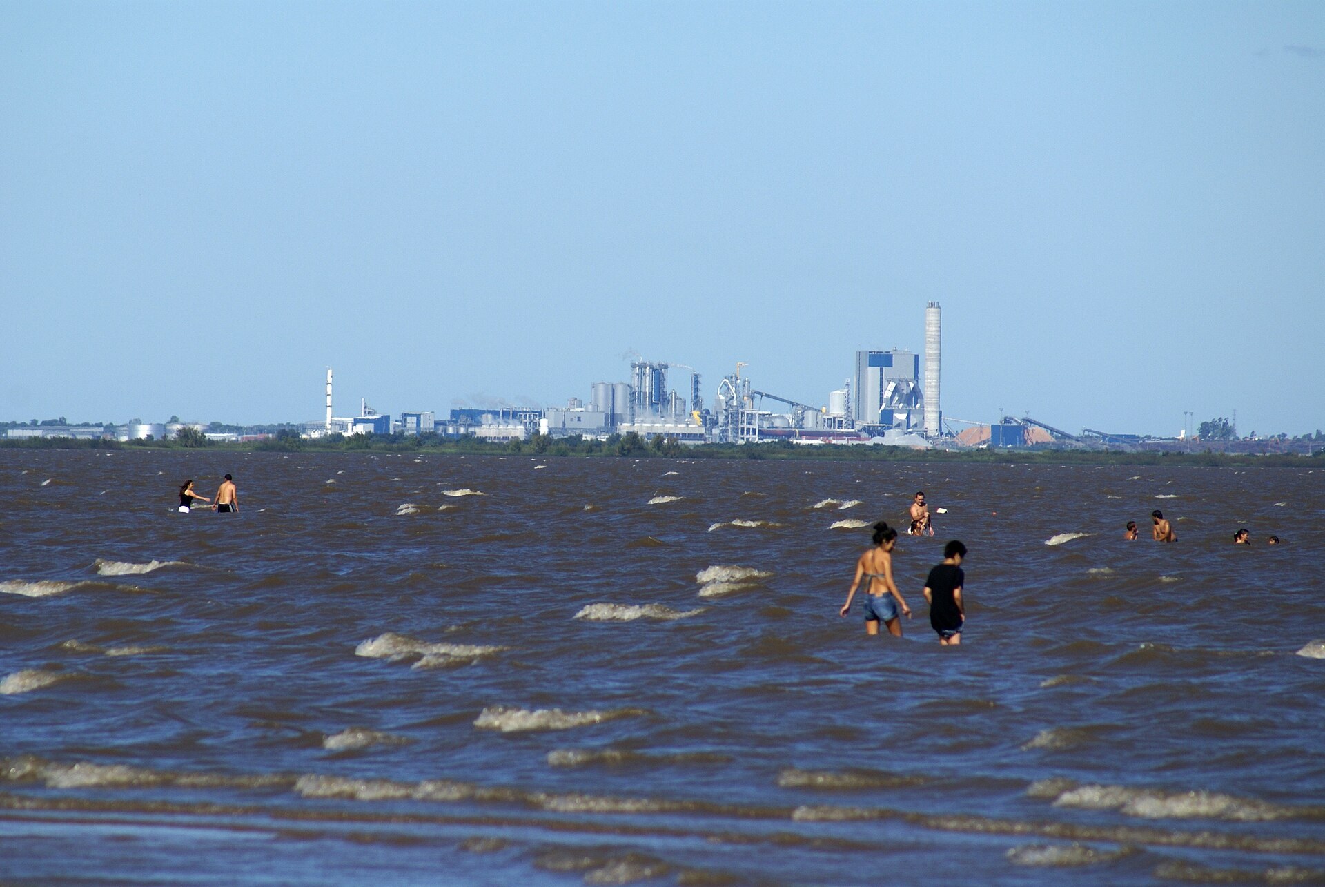 Pulp mill on the Uruguay River near Fray Bentos seen across the water with bathers in the foreground