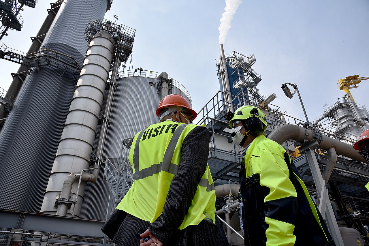 Two visitors in hard hats and high-visibility vests stand among steel towers and pipes at the UPM pulp mill in Fray Bentos, Uruguay