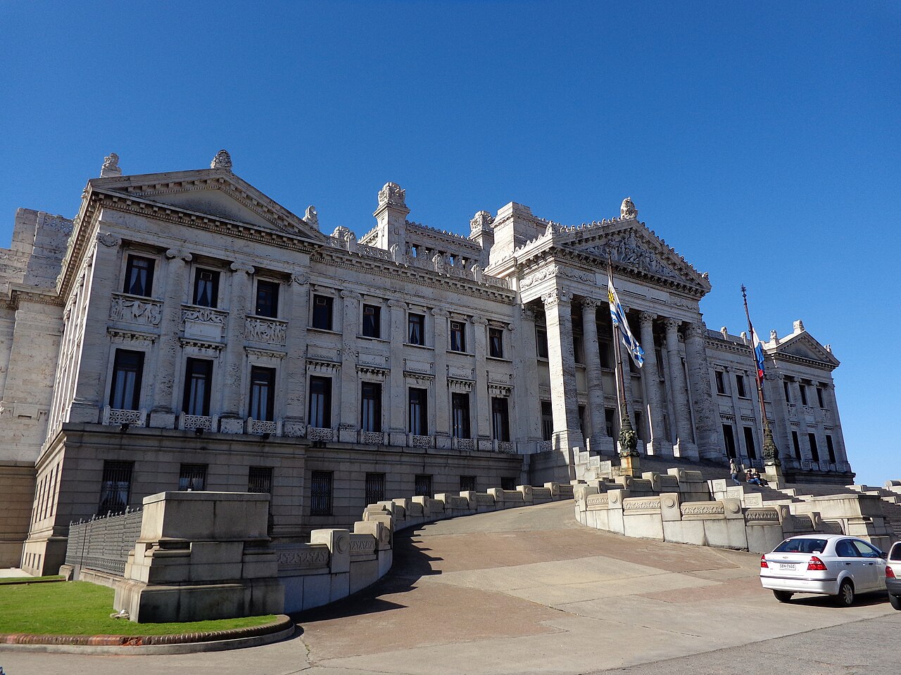 The white marble Palacio Legislativo in Montevideo under a clear blue sky, with a curved ramp, columns and the Uruguayan flag