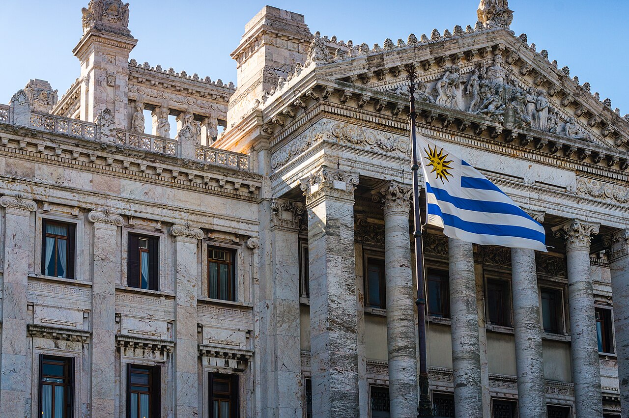 Marble columns and carved pediment of the Legislative Palace in Montevideo, with the Uruguayan flag flying against a blue sky