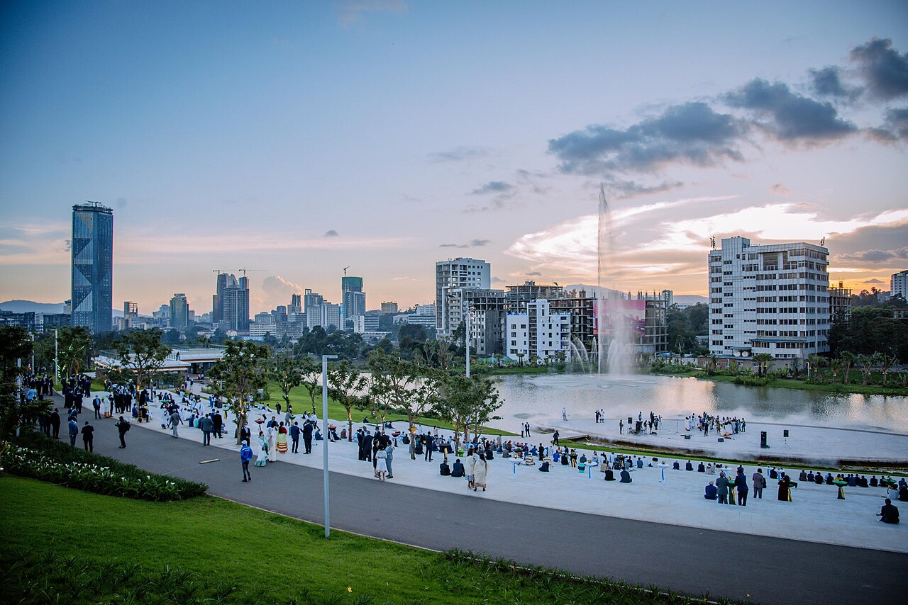 Skyline of Addis Ababa, Ethiopia, at dusk, with a lake, a fountain and crowds on a lakeside promenade
