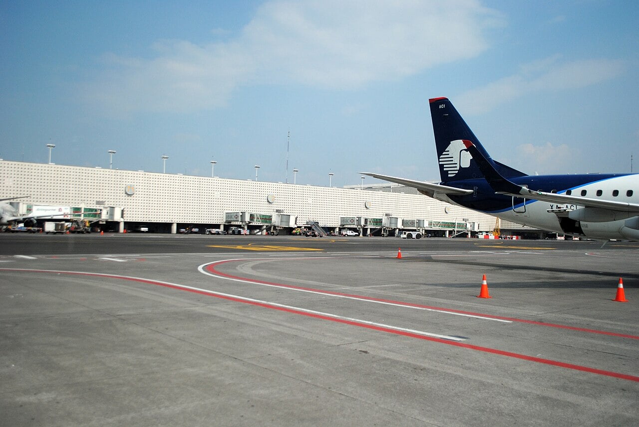 An Aeroméxico jet on the apron in front of the white facade and jet bridges of Terminal 2 at Mexico City International Airport