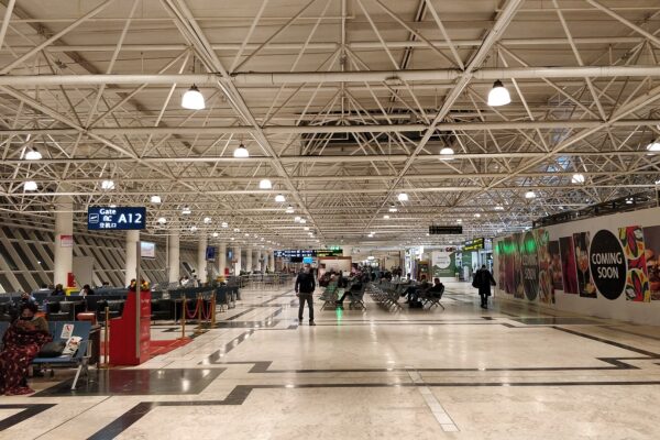 A long departures hall with white steel roof trusses and travellers seated near Gate A12 at Bole airport in Addis Ababa