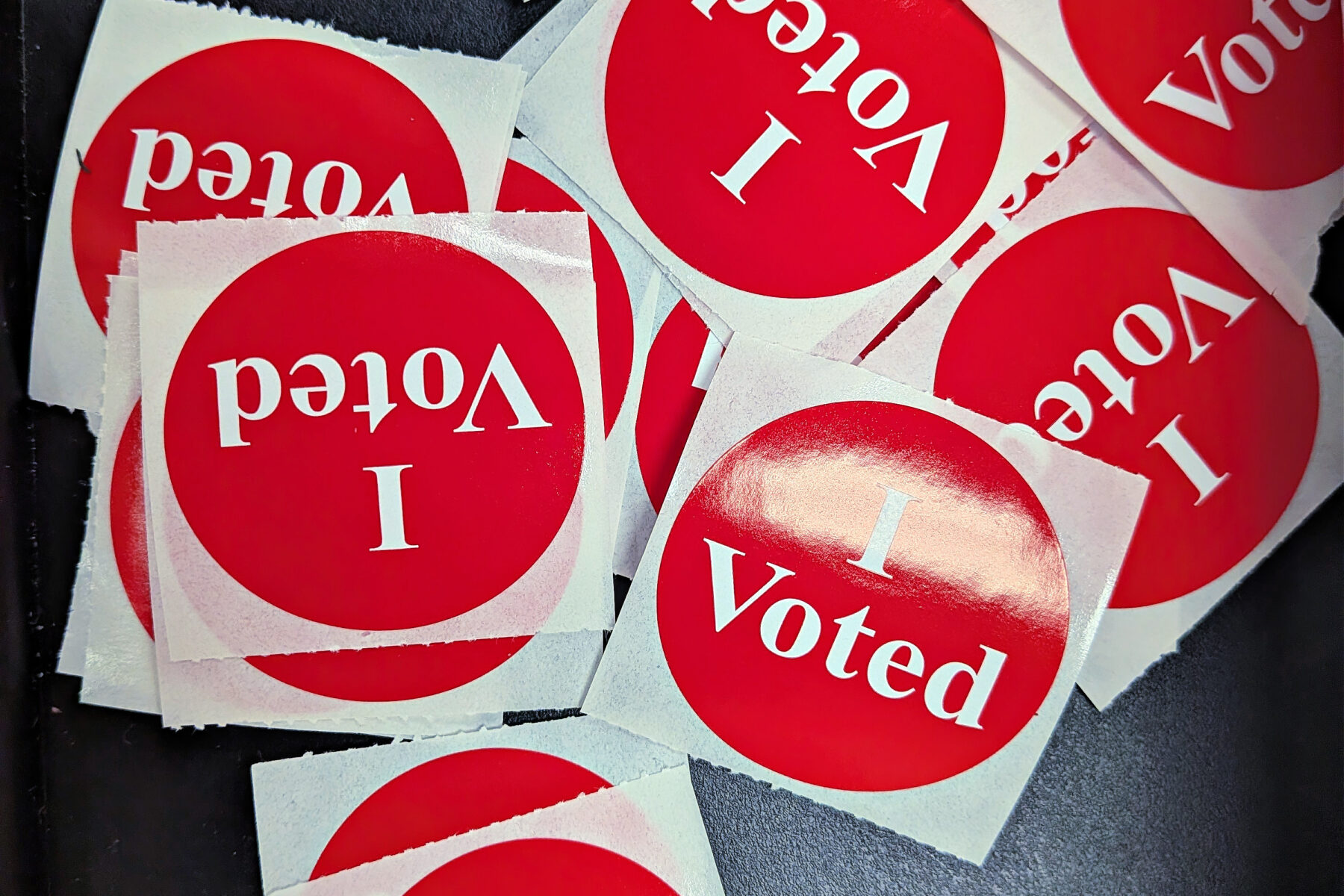 A pile of round red I Voted stickers on a dark table