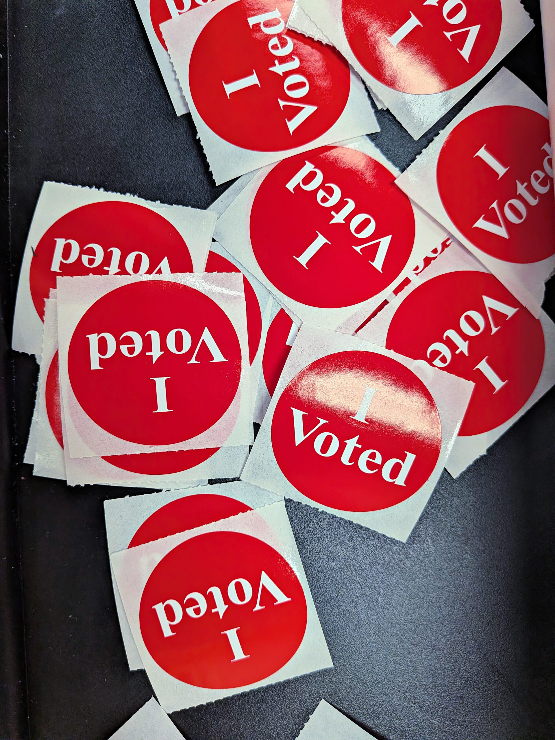 A pile of round red I Voted stickers on a dark table