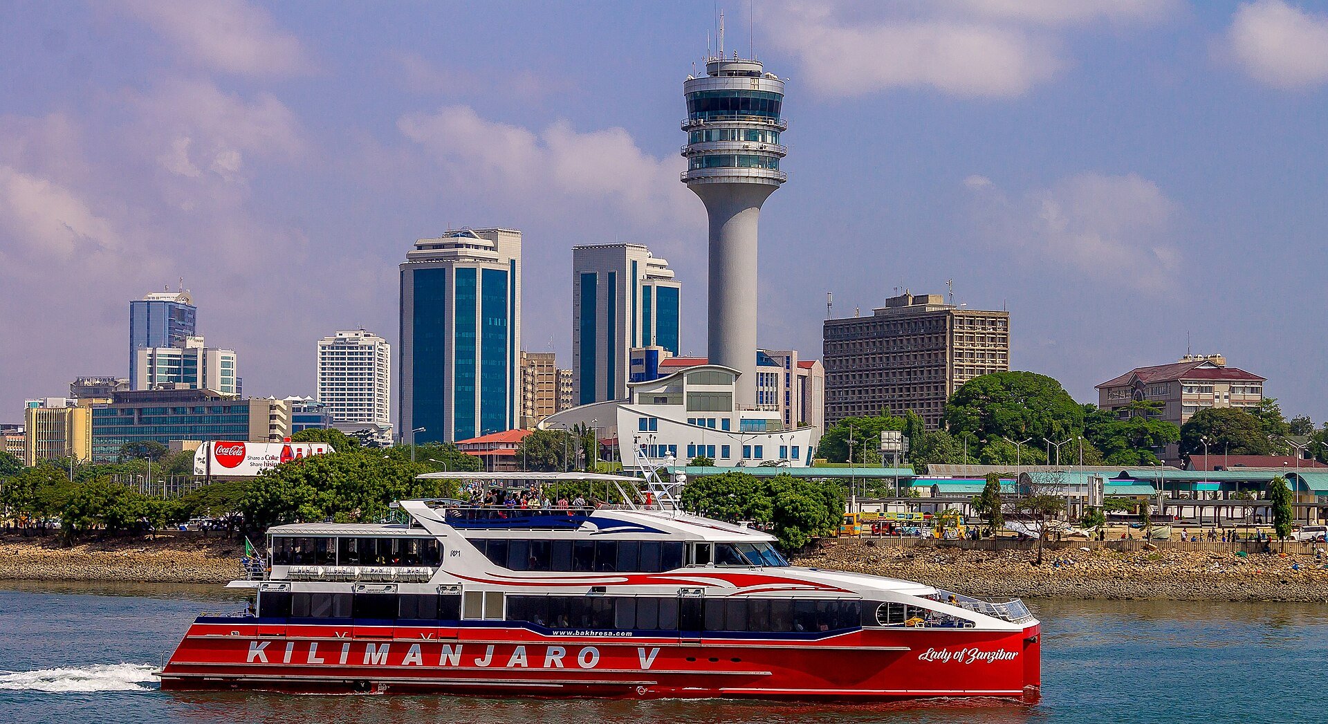 Downtown Dar es Salaam skyline with a red passenger ferry in the harbour and a tall tower behind the waterfront