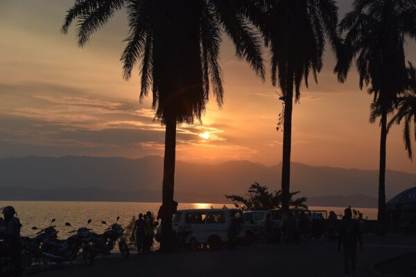 Sunset over Lake Kivu at Goma in eastern DR Congo, with palm trees, parked motorbikes and minibuses along the shore