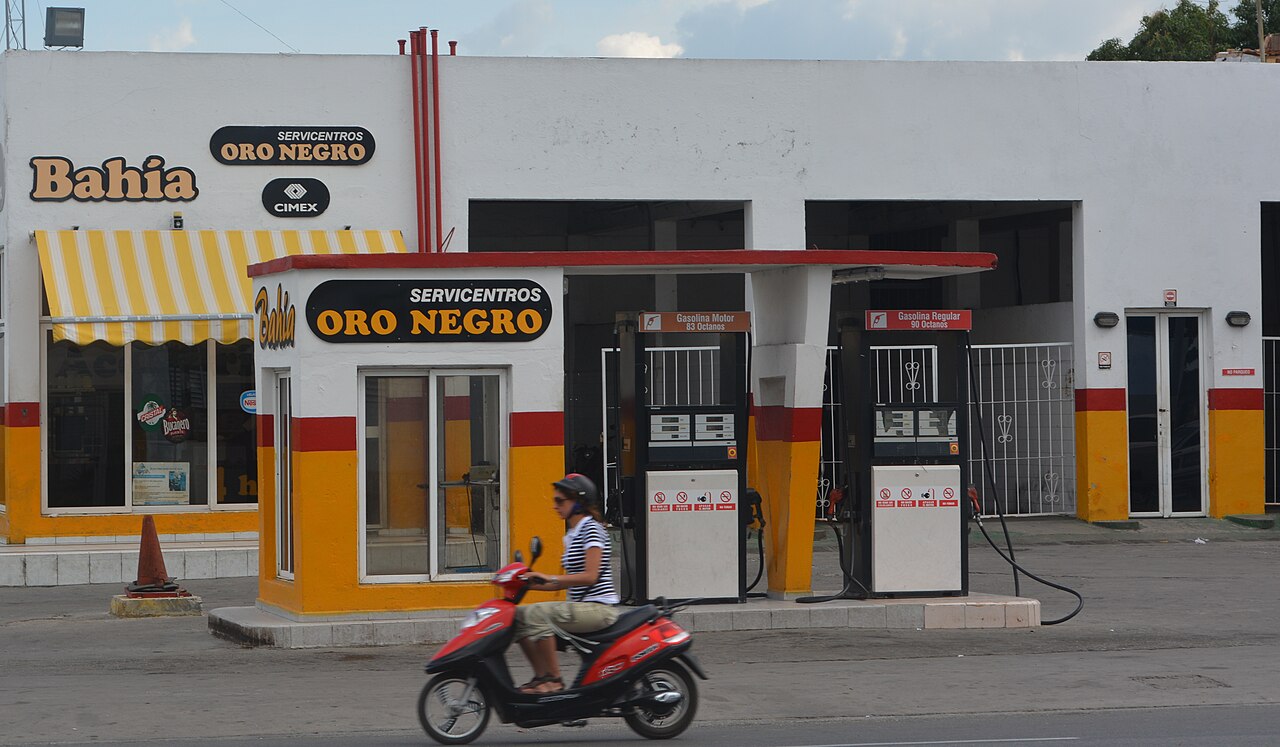 An Oro Negro petrol station in Cienfuegos, Cuba, with two fuel pumps and a woman riding past on a red scooter