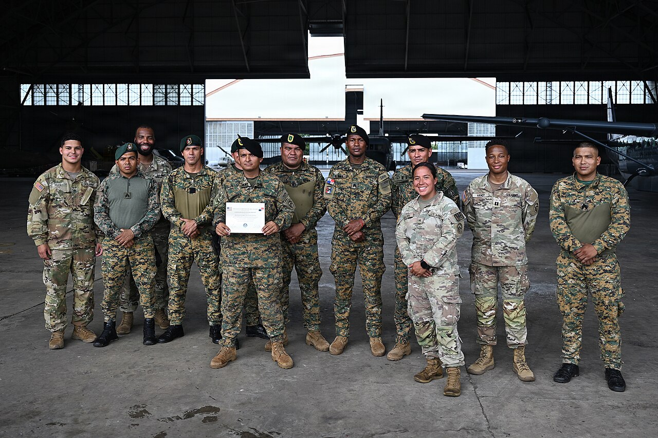 Panamanian Senafront officers in green berets and camouflage stand with US soldiers in an aircraft hangar, one holding a certificate.