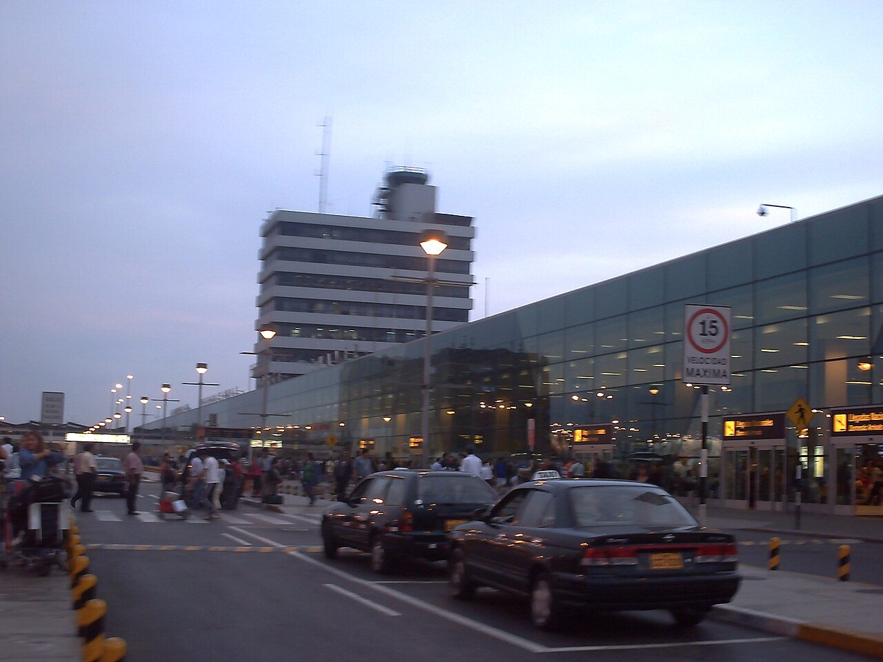 Exterior of the passenger terminal and control tower at Jorge Chávez International Airport in Lima at dusk, with taxis and travellers