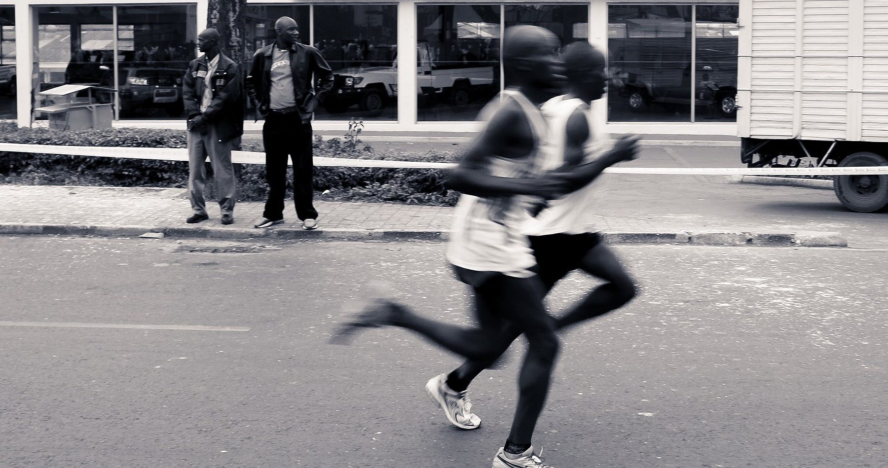 Two runners race past a car showroom while spectators watch from the pavement during the Nairobi Marathon