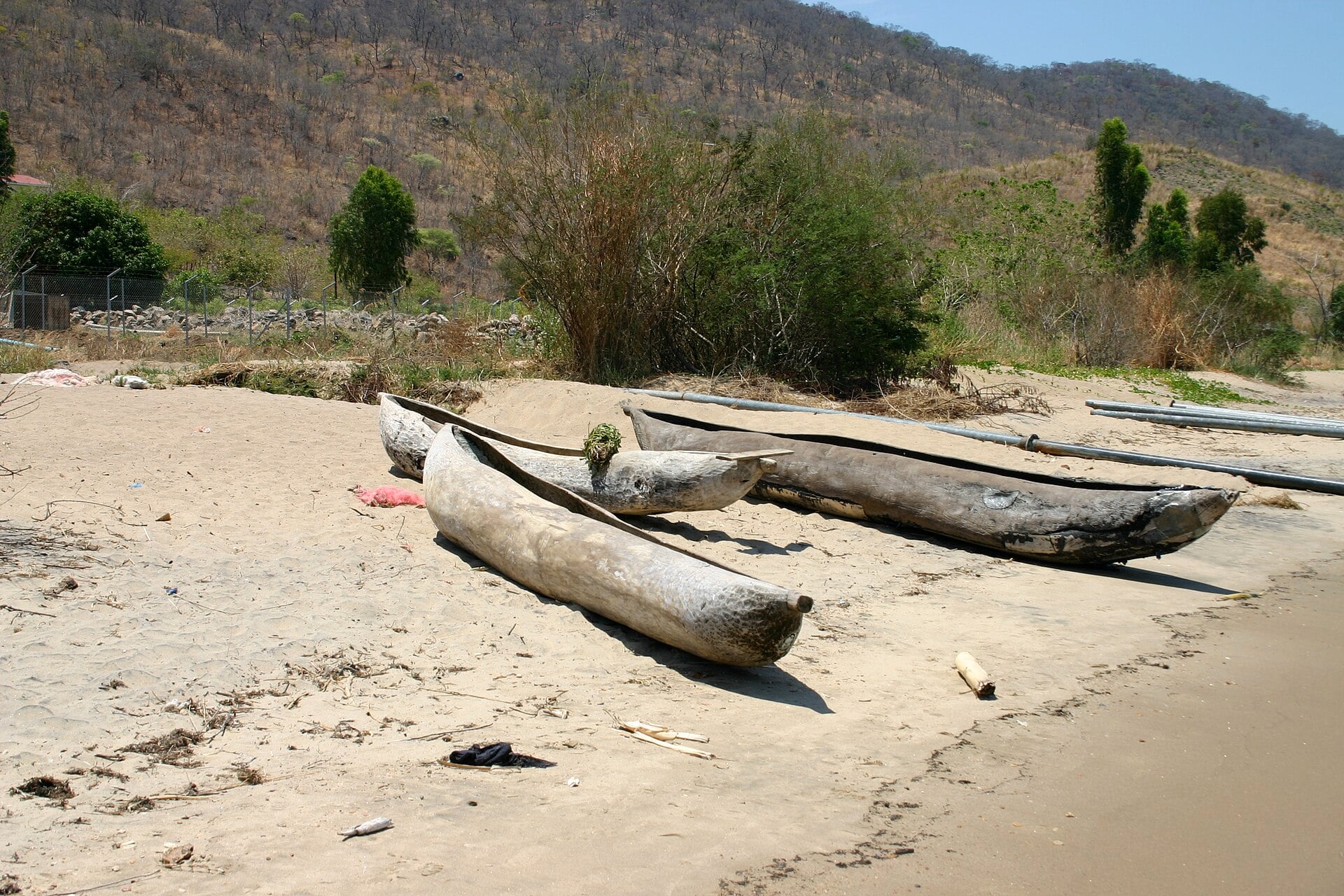 Three wooden dugout canoes resting on a sandy beach with dry hills behind