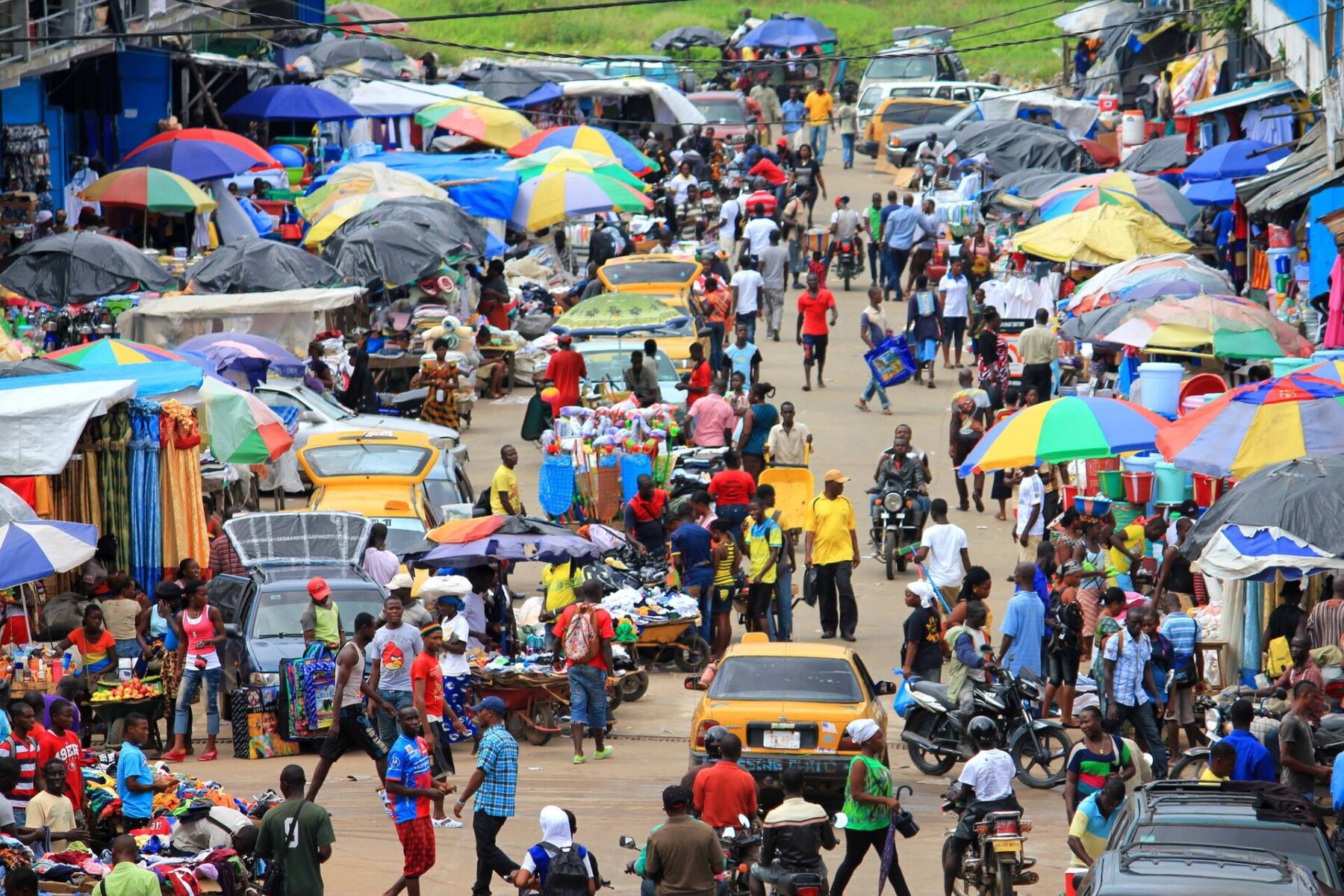 Crowded market street in Monrovia with colourful umbrellas, stalls, yellow taxis and pedestrians