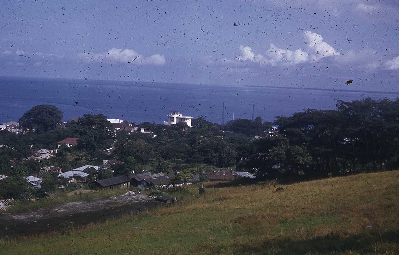 View over green hills and rooftops of Freetown towards the white State House building and the Atlantic Ocean