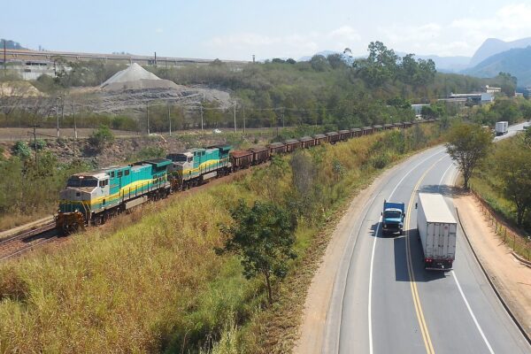 A Vale iron ore train with green and yellow locomotives runs beside the BR-381 highway near Timóteo, Minas Gerais