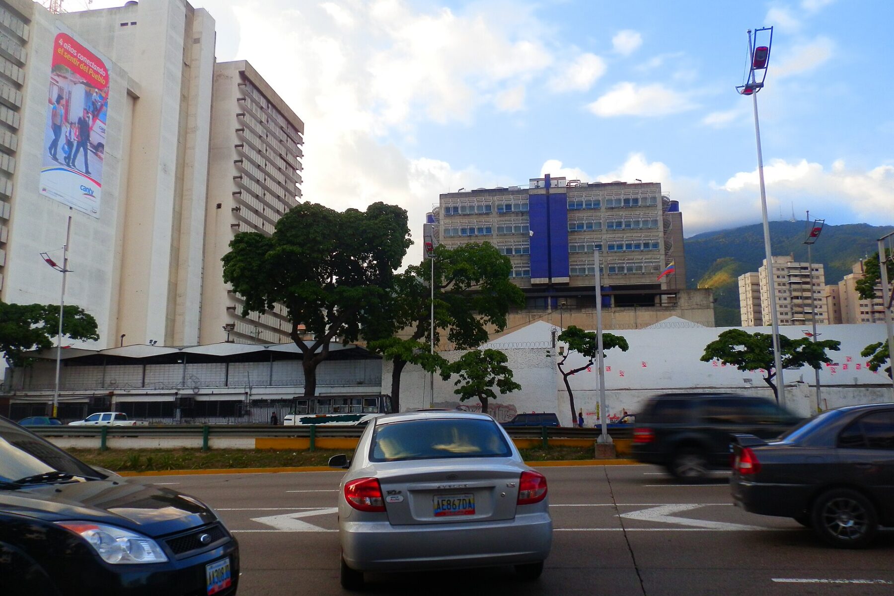 A CANTV banner on a telecoms building with rooftop antennas beside a Caracas avenue