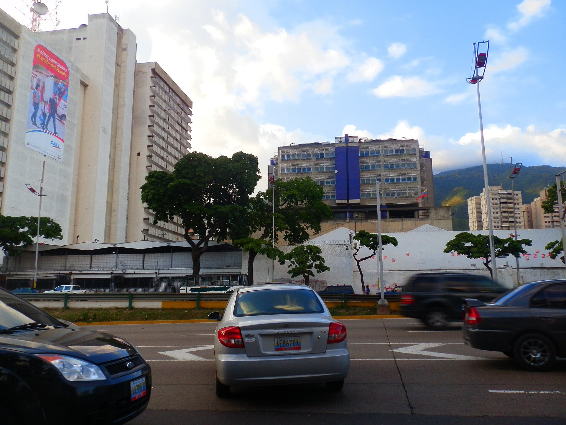 A CANTV banner on a telecoms building with rooftop antennas beside a Caracas avenue
