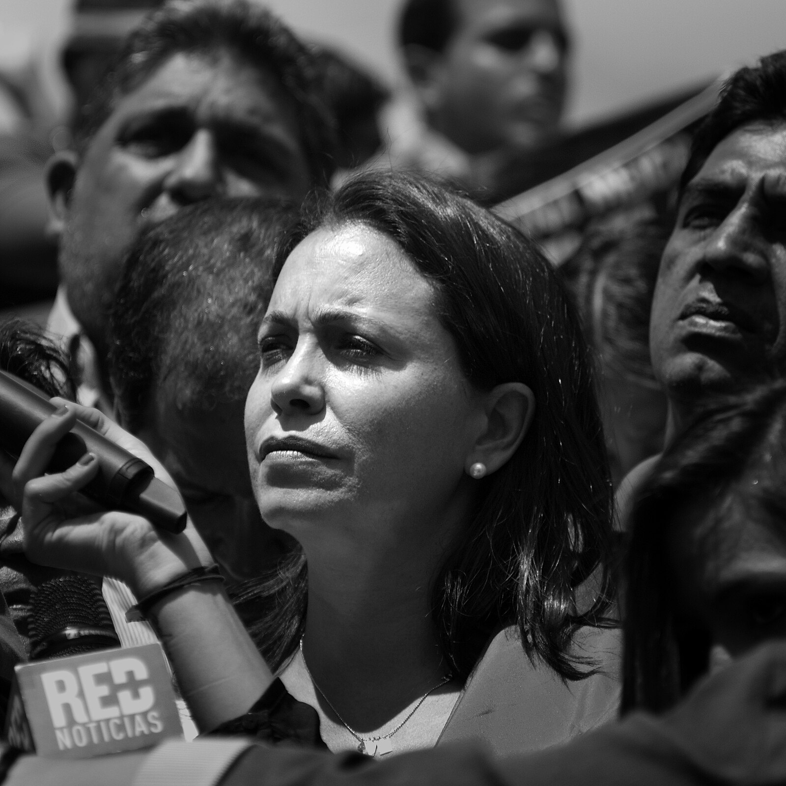 Black-and-white portrait of María Corina Machado speaking to reporters at a protest in Caracas, Venezuela