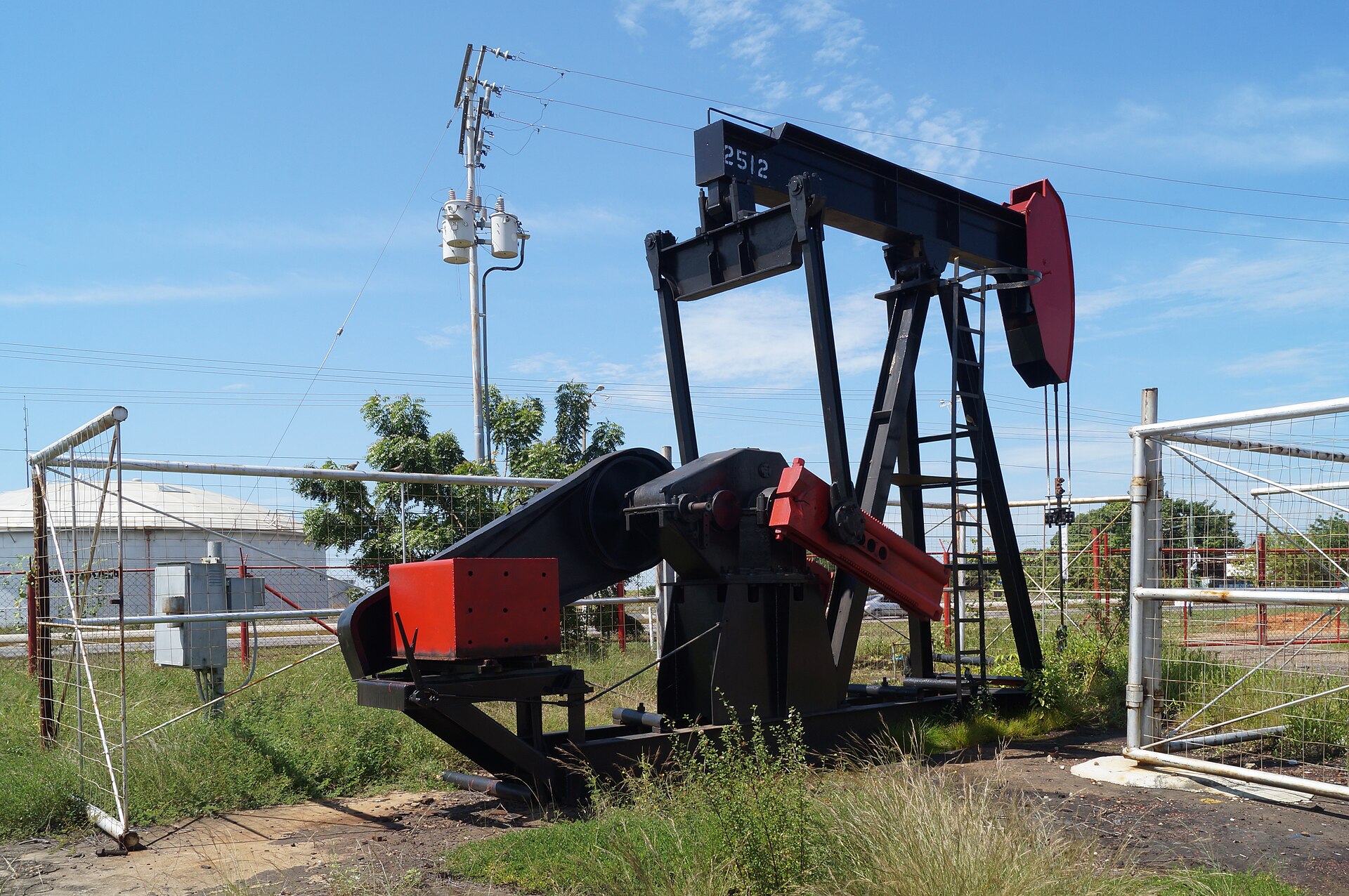 Black and red oil pumpjack at a fenced well site in Lagunillas municipality, Zulia state, Venezuela