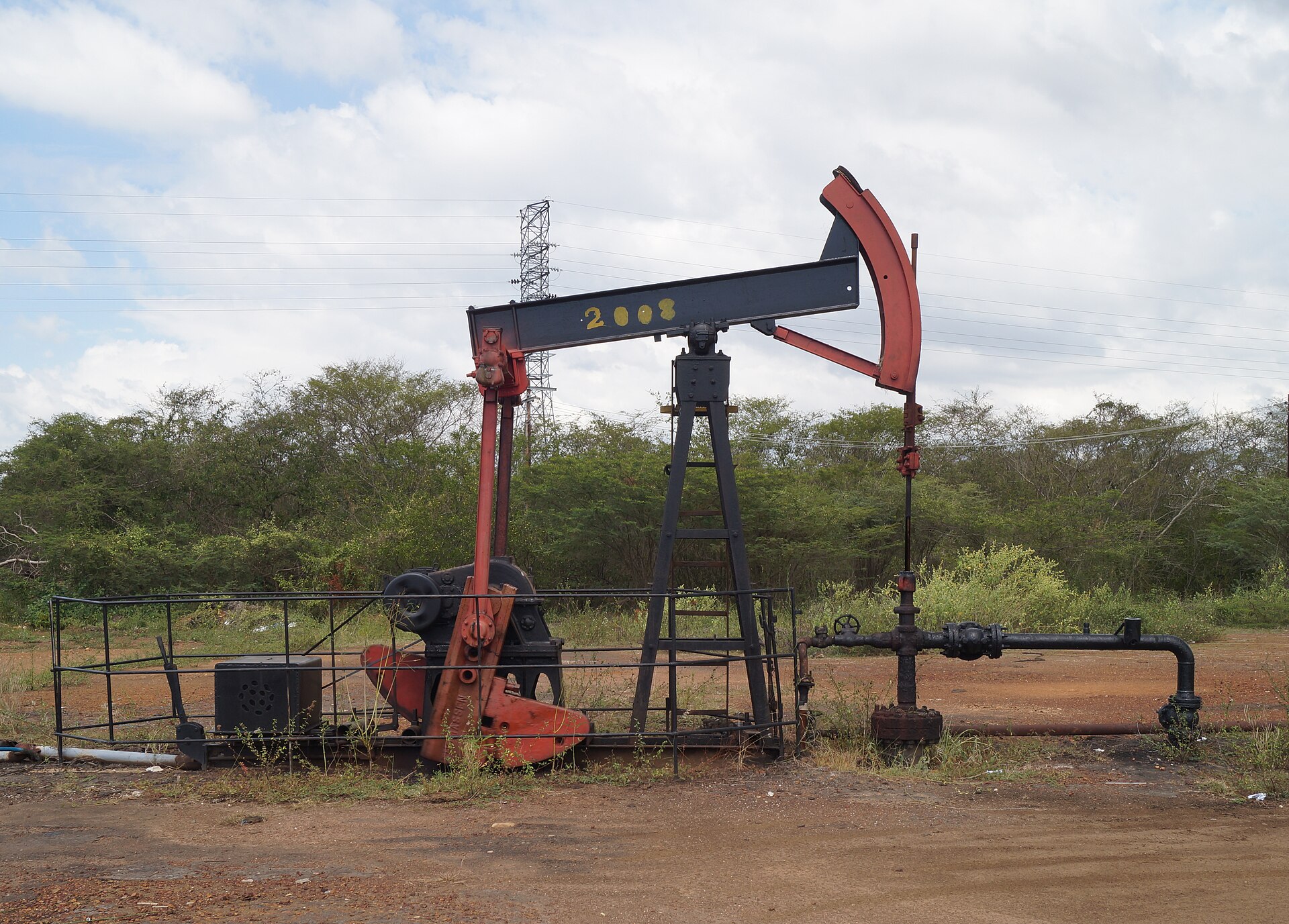 Red and black oil pumpjack and wellhead on dry land in Zulia state, Venezuela