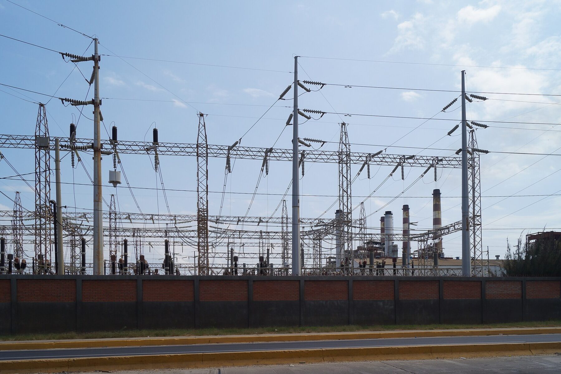 High-voltage power lines and a substation in Maracaibo, Venezuela, with the chimneys of a power plant in the background