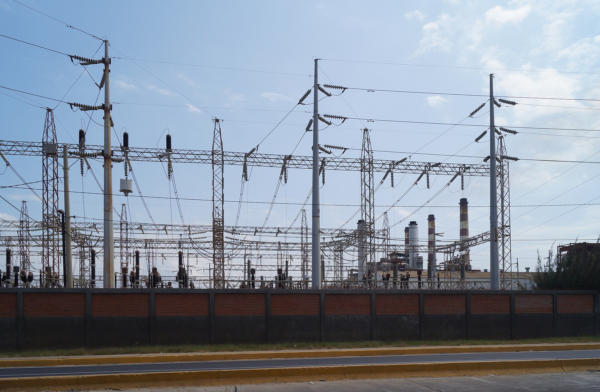 High-voltage power lines and a substation in Maracaibo, Venezuela, with the chimneys of a power plant in the background