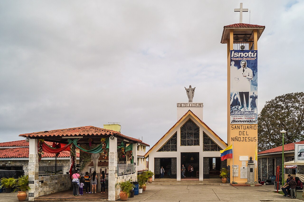 A small church with a tall yellow bell tower in Isnotú, with a banner showing a man in a white coat and the words Santuario del Niño Jesús.