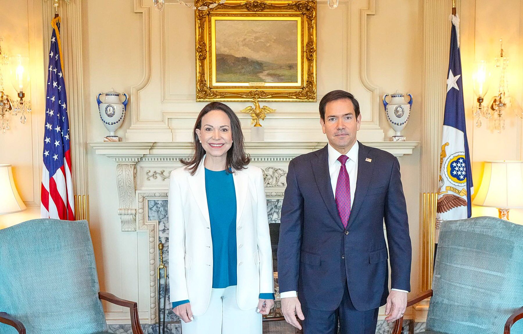 María Corina Machado, in a white suit, stands beside US Secretary of State Marco Rubio in a formal State Department reception room